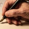 An older person's hand writing in cursive on cream paper with a fountain pen