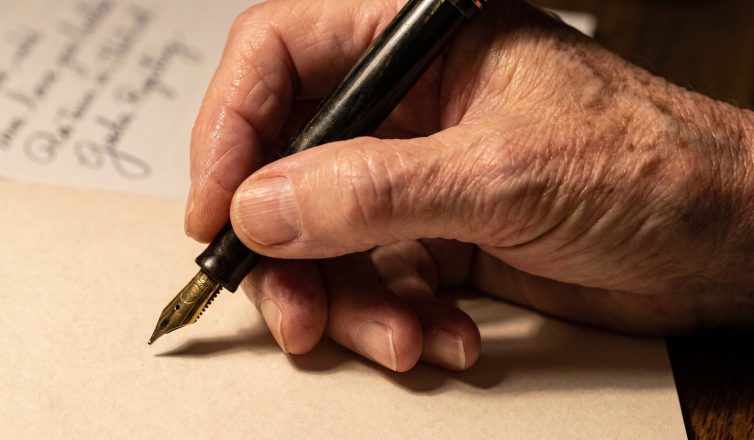 An older person's hand writing in cursive on cream paper with a fountain pen