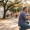 A father kneels to greet his son at afternoon school dismissal under live oaks outside a limestone Texas elementary school